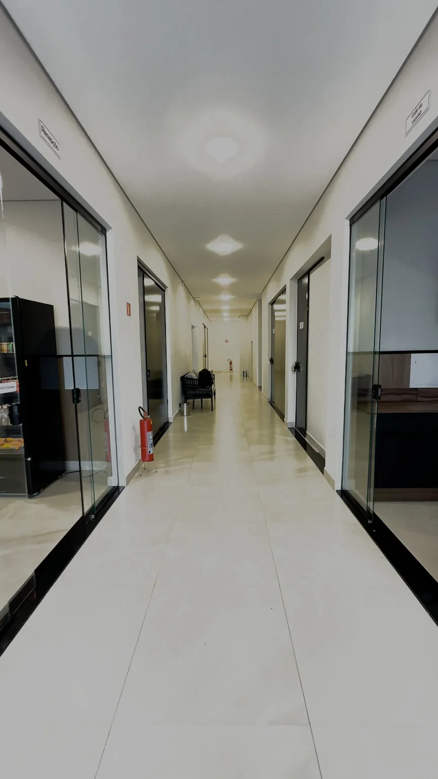 Corredor interno iluminado com portas de vidro junto à recepção e ao salão