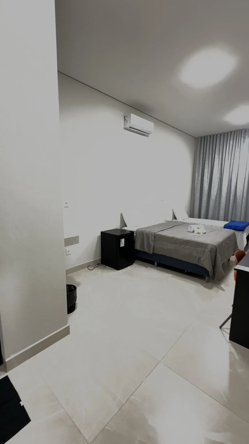 Quarto com cama de casal, cortina cinza, ar-condicionado e mesa de apoio