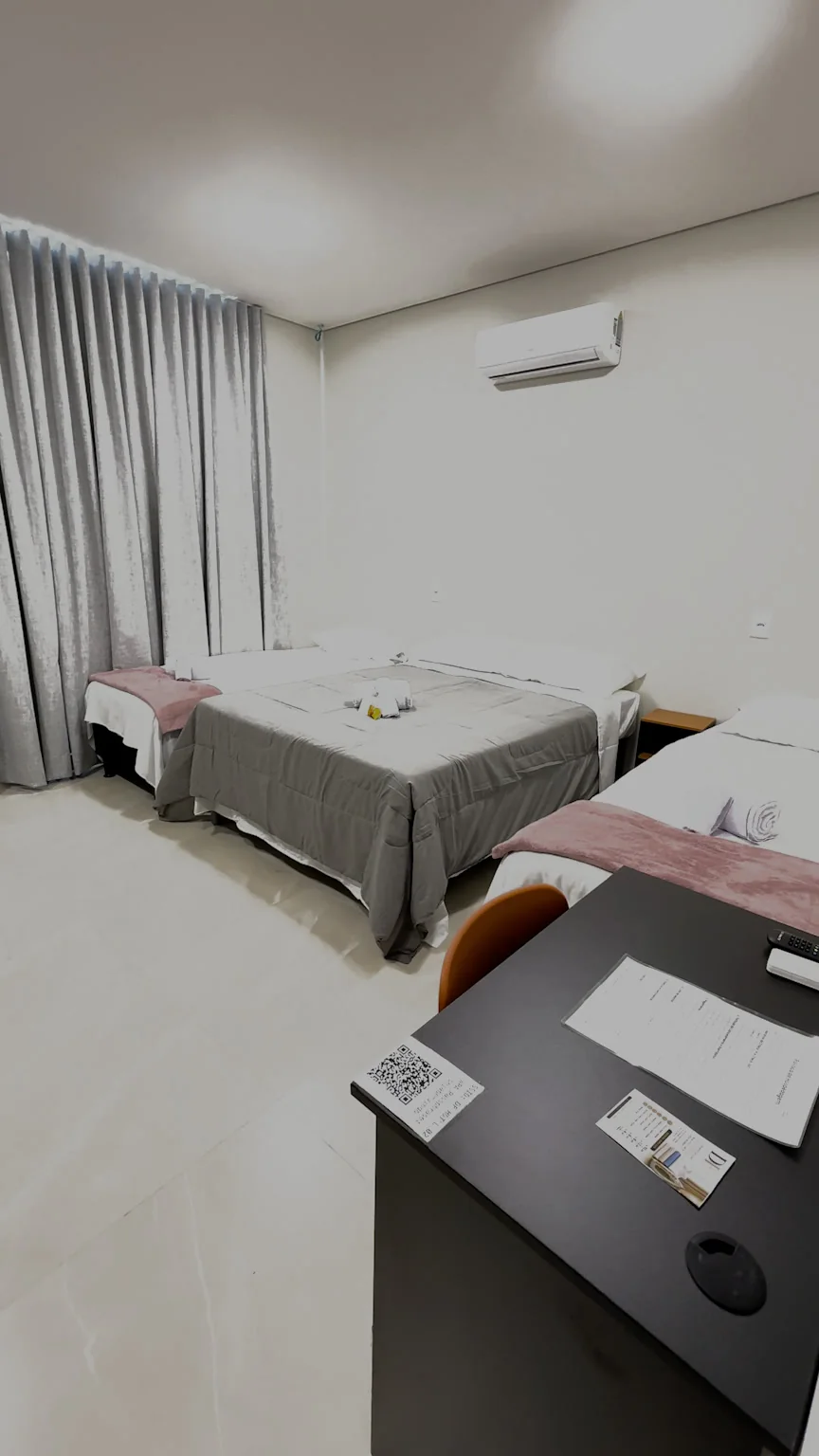 Acomodação com cama de casal e camas de solteiro, cortina cinza e mesa